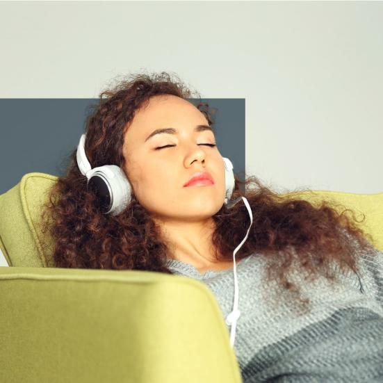 Kvinde sidder lænet tilbage i en sofa med lukkede øjne med hovedtelefoner på