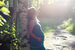 Gravid kvinde støtter sig op af træ og ser eftertænksom ud