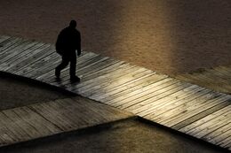 Sortskygget person går på et plankeværk i mørket