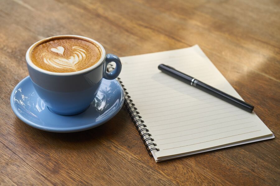 en lækker kop kaffe med en kuglepen og notesblok liggende ved siden af
