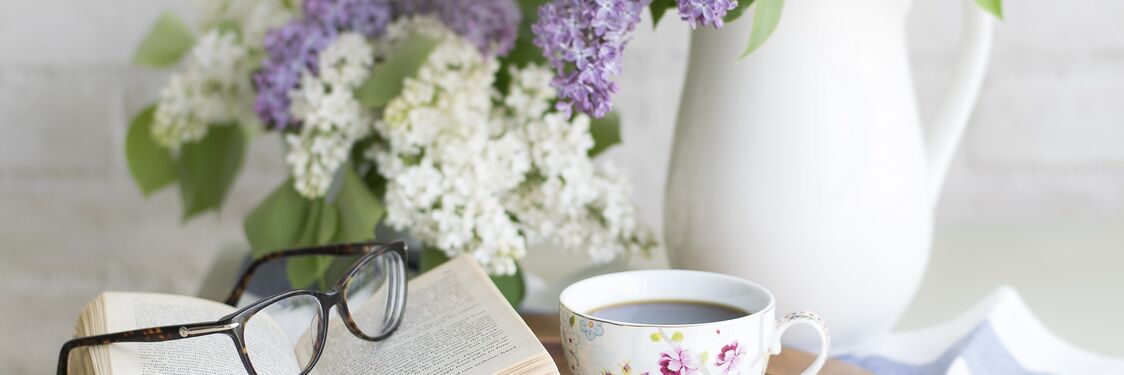 cafebord med en bog, en kop kaffe og en vase med blomster
